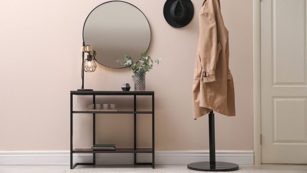 door with raised mouldings next to a mirror and coat stand with trench coat draped over it